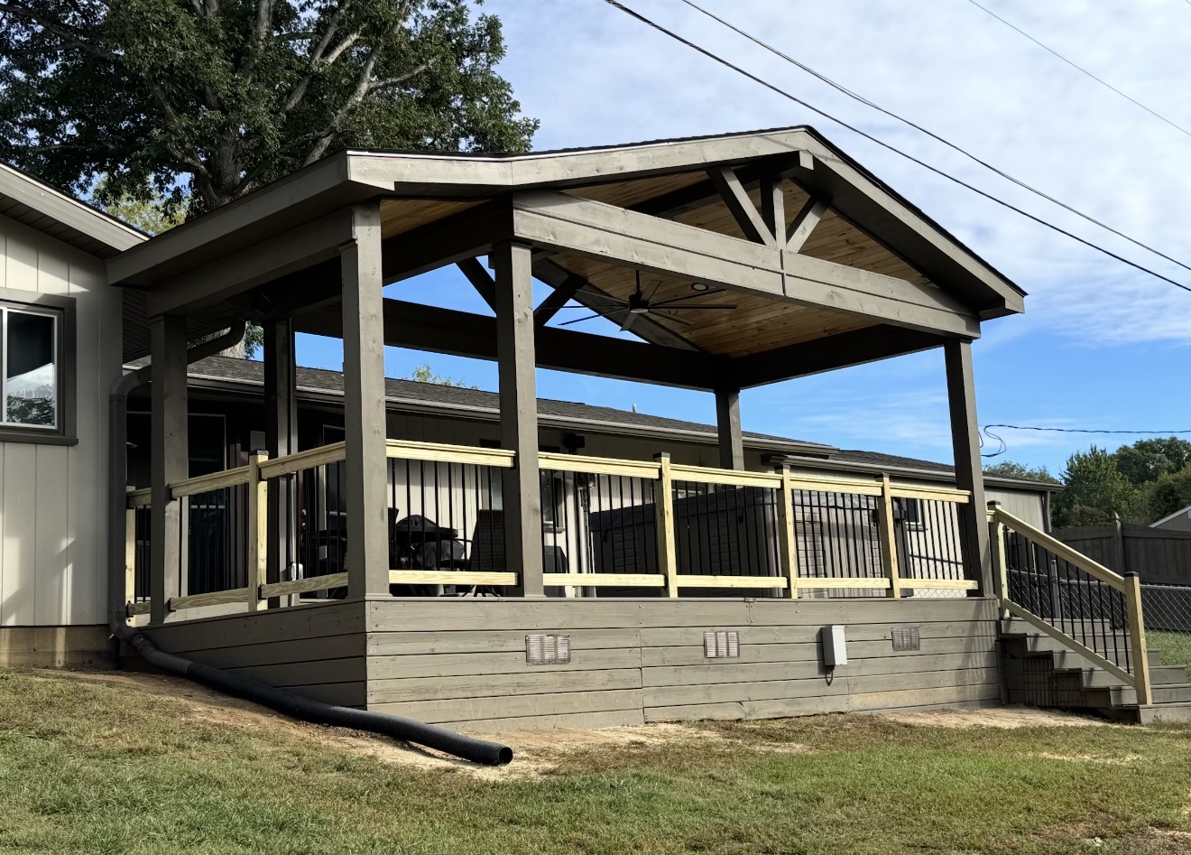 Covered deck with gable roof, wood posts, black railing balusters and skirting