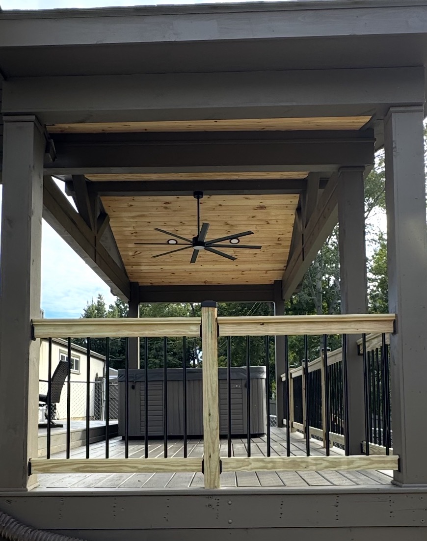 Covered deck ceiling with fan above a hot tub and wood railing
