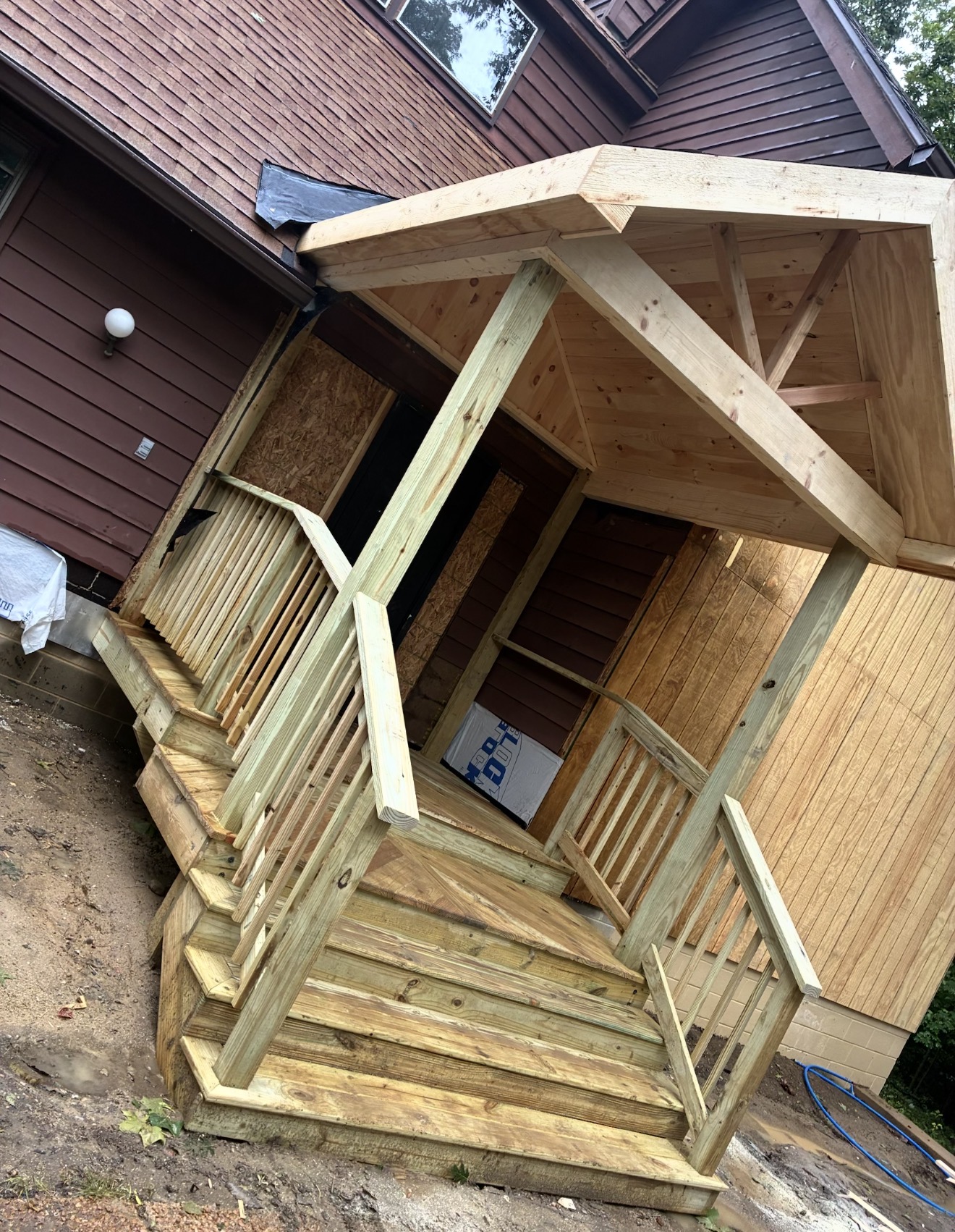 Covered wood entry porch with posts, railings and stairs